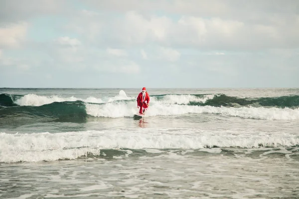 Ung mann surfer utkledd som julenisse på stranda – stockfoto