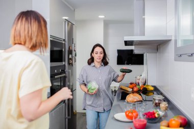Basit sağlıklı yiyecek konsepti. Neşeli arkadaşlar ev mutfağında sebze salatası pişiriyor.