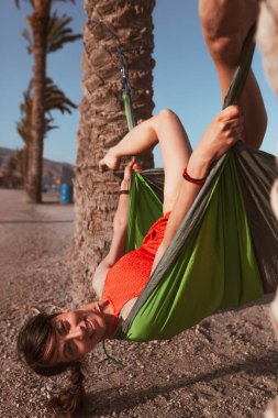 Sahildeki palmiye ağaçları arasında hamakta yatan kadın.