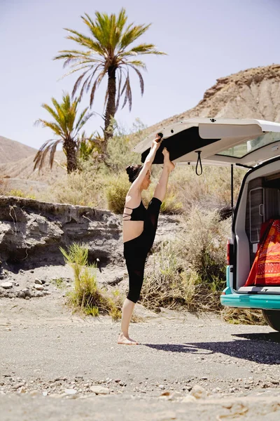 Young active woman practicing yoga in desert on sunny day, with a campervan