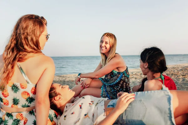 Mujeres jóvenes tumbadas en la playa, sonriendo y hablando sobre una bufanda grande — Foto de Stock