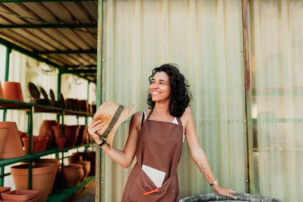 Kvinna fläktar sig själv med sin halmhatt vid dörren till hennes keramiska verksamhet — Stockfoto