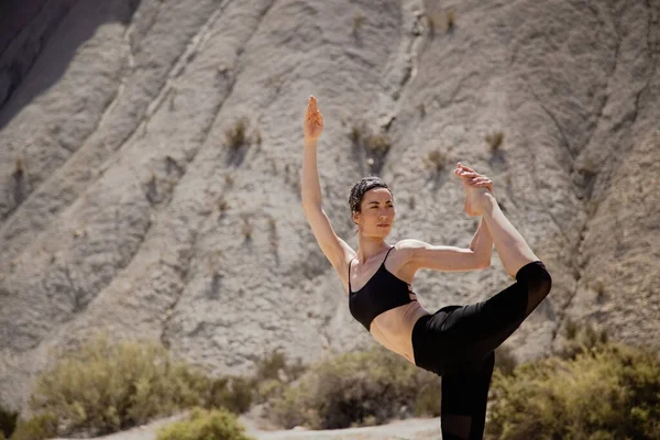 Young active woman practicing yoga in desert on sunny day, health and active life concept