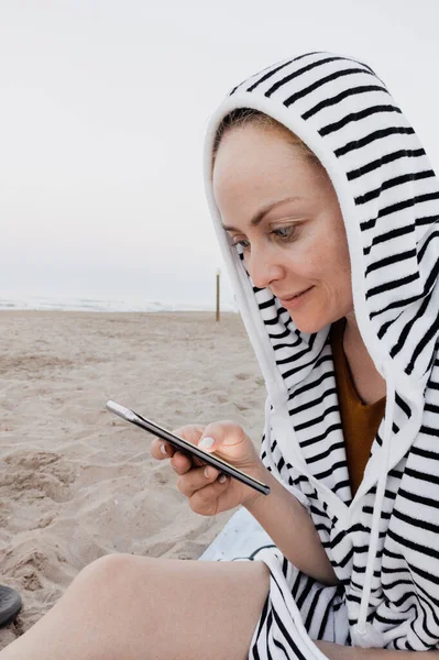 Femme utilisant son smartphone à la plage avec towell crochet — Photo