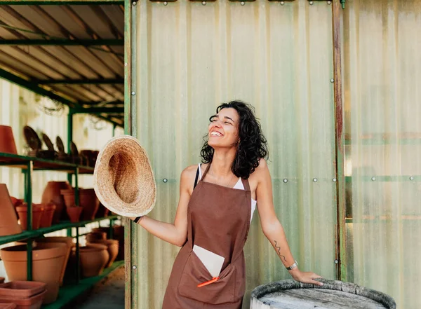 Woman fans herself with her straw hat at the door of her ceramic business — Stock Photo, Image