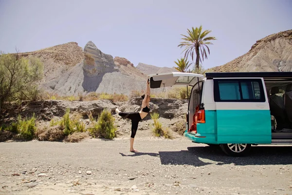 Young active woman practicing yoga in desert on sunny day, with a campervan