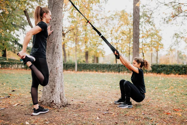 Women training with trx outside in the park.