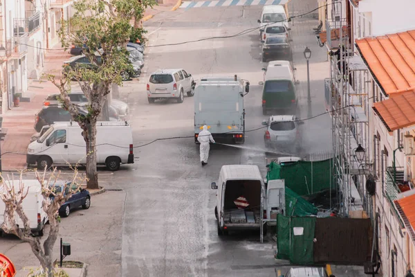 Sanitation worker in hazmat protection suit with chemical decontamination sprayer truck.