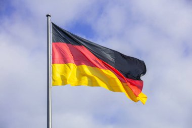 Alman bayrağı bayrak direği üzerinde sallayarak. Birçok bulutlar arka plan ile mavi gökyüzü.