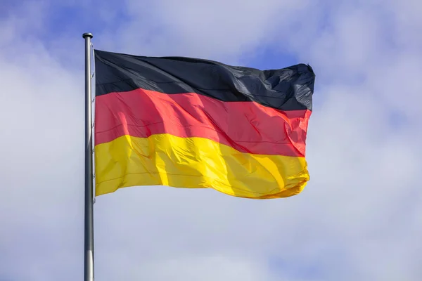 Duitse vlag zwaaien op zilveren vlaggenmast. Blauwe hemel met veel wolken achtergrond. — Stockfoto