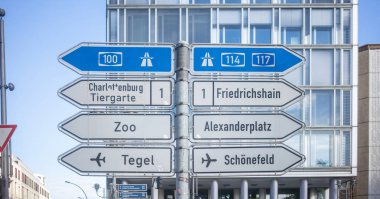 Oklu tabelalar Berlin, Almanya'nın ana yönlerini gösterir. Mavi gökyüzü ve cam pencere bina arka plan.