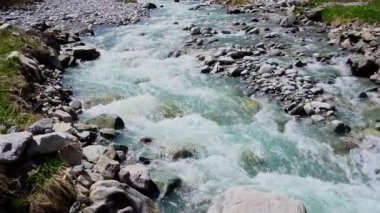 Ağır çekim. Berrak turkuaz suyla Ala-Archa Nehri 'ne akıyordu. Kayalar ve kayalar, dağlık alan. Yürüyüş, yürüyüş, dağcılık, sırt çantası, macera için ideal.