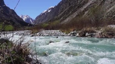 Akan bir turkuaz ağır çekim Ala-Archa nehri engebeli bir dağ vadisini kesiyor. Kayalık arazi ve uzak karlı zirveler, açık hava macerası, yürüyüş ve alp keşfi için ideal..