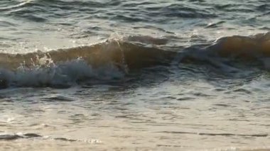 Gün batımında deniz kıyısına küçük dalgalar vuruyor.