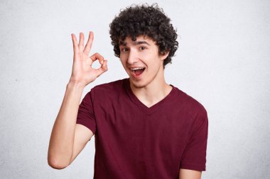 Her şey yoluna girecek! Memnun kıvırcık adam emin ve mutlu bir ifadeyle görünüyor, ok işareti gösterir, onun hazırlık ve farkındalık, beyaz arka plan üzerinde izole rahat t gömlek giymiş gösterir