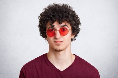 Headshot serin şık sakallı genç erkek kıvırcık saçlı giyer moda kırmızı yuvarlak gözlük, tarihi, onun kız arkadaşı geç, pozlar beyaz arka plan karşı olduğu gibi şaşkın için hazır.