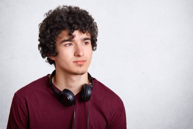 Kıvırcık erkekle düşünceli düşünceli ifade, modern kulaklıklar var, distnace ikindilerde görünüyor, boş zaman yalnız geçiriyor, metniniz için boş kopya alanı ile beyaz arka plan teşkil etmektedir