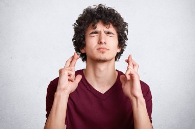 Yakışıklı bir adam portresi kıvırcık saçlı, gözleri kapanır, parmak geçerek, dilek yapar, rahat t gömlek giyer, beyaz duvara teşkil etmektedir. Genç final sınavı sonuçlarını jest dua yapar bekliyor.