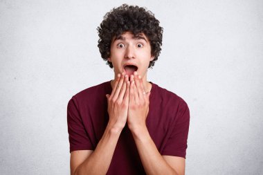 Fotoğraf hayretler içinde erkek genç, çene, ellerinde tutar ağız yaygın olarak açılan, kötü haber, hayrete karşı beyaz beton zemin teşkil etmektedir. Şaşırmış şaşkın Avrupa hipster kapalı duruyor