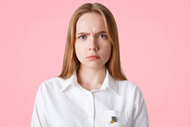 Çok güzel genç kadın, kasvetli ifade, portresi yüz frowns, uzun saçlı, sağlıklı cilt, mavi gözlü, beyaz gömlek, pembe bir arka plan üzerinde pozlar. Şikayetçi kadının erkek arkadaşı ile bir sorunum var