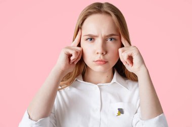 Headshot konsantre Avrupa kadın modeli, işaret parmakları tapınak üzerine tutar, kamera, pembe bir arka plan üzerinde izole ciddi bakar. Gerekli bilgileri hatırlamak ciddi kadın öğrenci çalışır