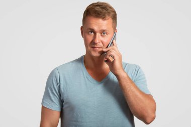 Yakışıklı genç işadamı emin ifadeyle, modern cep telefonu tutan, beyaz arka plan üzerinde izole rahat mavi t gömlek giymiş biri ile iletişim kurar. İletişim kavramı