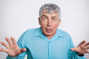 Korkmuş olgunlaştı buruşuk erkek olumsuz duyguları ifade eder, jestler ve görünümü ile kamera, beklenmeyen ifadeye giyer resmi gömlek, beyaz arka plan üzerinde izole. Yüz ifadeleri kavramı