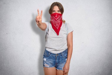 Kendini kadın feminist barış işareti, gösterir emin kapalı atış moda kırmızı bandana giyer, şort ve gri arka plan üzerinde izole gri t gömlek giyer. Bütün kadınların erkeklerle eşit olduğunu