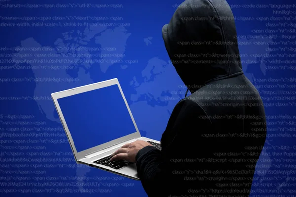 Anonymous faceless hacker in black clothing stands back, works on code on laptop computer, isolated over dark blue interface background. Internet crime concept. Hacker steals data, breaks access
