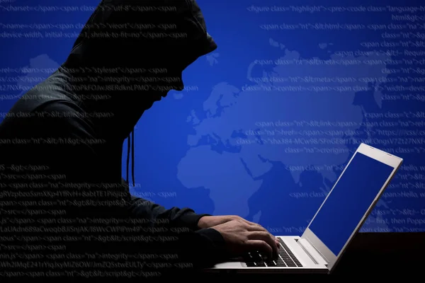 Dangerous male hacker in black hoody works hard on solving online password code on laptop computer, keyboards information, tries to break system, poses sideways against dark binary streams background