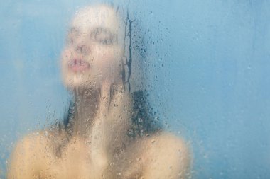 Çıplak kadın modeli alır duşa kabin odaklanmamış silüeti rahat hissediyor ve vücudu kadın yıkar ağlayan cam duş kapının arkasında önemser. Alma banyo. Cilt bakım kavramı