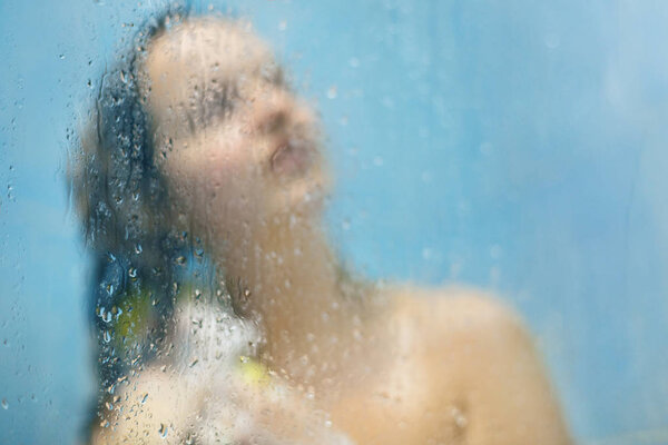 Обнаженная молодая женщина модель имеет мягкую здоровую кожу, моет волосы и тело с шампунем и гелем для душа, принимает душ в ванной комнате, выступает против пота росы размытый фон с капли воды
