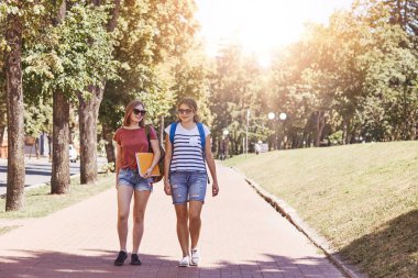 Geri okul kavramı. İki kız öğrenci vardır yürüyüş açık, sırt çantası ve Kitaplar, yazlık giysiler ve tonları giymiş, üniversite veya kolej haberler son eaxam için hazırlık tartışmak