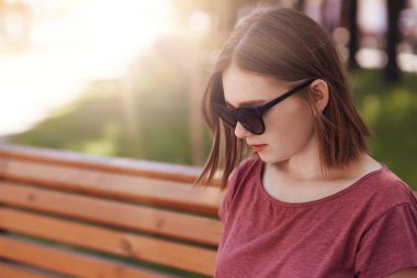 Tonları, güzel genç kadın modelinde trendy saç kesimi vardır, okuma, odaklı bankta oturur ya da bir şeye benziyor, güneşli yaz hava sahiptir, ciddi ifade ve iyi dinlenme açık vardır