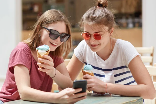 Mutlu kadın arkadaşları odaklı Ino ekran modern cep telefonu, ilginç video online, seyretmek olmak kablosuz internet'e bağlı kayıtsızca giyinmiş soğuk dondurma yemek memnun. Arkadaşlık