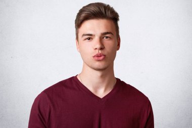 Portre yakışıklı ciddi erkek genç trendy saç kesimi, sağlıklı cilt vardır, dudakları Gücenmek ve kendinden emin bir ifadeyle görünüyor, rahat t gömlek giyer, beyaz arka planı teşkil etmektedir. İnsanlar ve gençlik