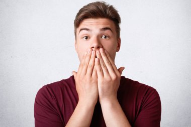 Şaşkın güçlü erkek yatay atış ellerle ağız kapakları, surprisement, recives unexecpected haber intelocutor, beyaz beton duvardan izole görünür. Yüz ifadeleri kavramı