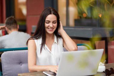 Dişlek gülümseme neşeli genç kadın serbest meslek Bistro dizüstü bilgisayarda çalışır, beyaz bluz, kablosuz wifi internet web sayfası bağlı Gözatma sayısı içinde çalışmayı, bitireceği gibi giyinmiş. Teknoloji kavramı