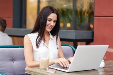 Genç ve güzel kadın yöneticisi hoş gülümseme yüzünü, kahve dükkanında yemek molası sırasında sosyal ağlarda sohbet etmek mutlu vardır, yüksek hızlı internet bağlantısı sahiptir. İnsanlar, duygu ve boş zaman etkinlikleri