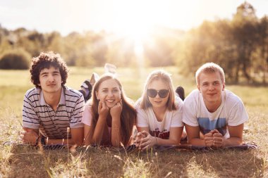 Çimenlerin üzerinde mutlu ifade yalanla dört arkadaş sevindim, çeneleri tutun ve positvely kameraya bak, güneş keyfini çıkarın, iyi dinlenme gibi boş zaman açık harcamak zorunda. Gençler, gençler ve yaşam tarzı kavramı