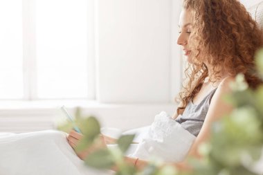 Çok kıvırcık çekici genç hanım Pijama içinde giyinmiş yana doğru atış erkek arkadaşıyla mesajlaşma için modern cep telefonu kullanır, Pazar sabahı, rahat yatak odası iç üzerinde pozlar sırasında yatakta kalır