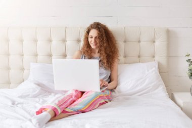 Laptop yatakta, pijama, giyinmiş güzel kadın işleri sahiptir konfor, evde olmak, bağlı yüksek hız memnun internet, dostu olumlu gülümseme vardır. İnsanlar, teknoloji, eğlence kavramı