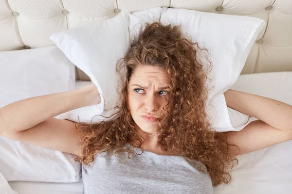 Pretty Discontent Female Curly Covers Ears Pillow Lies Bed Has — Stock Photo, Image