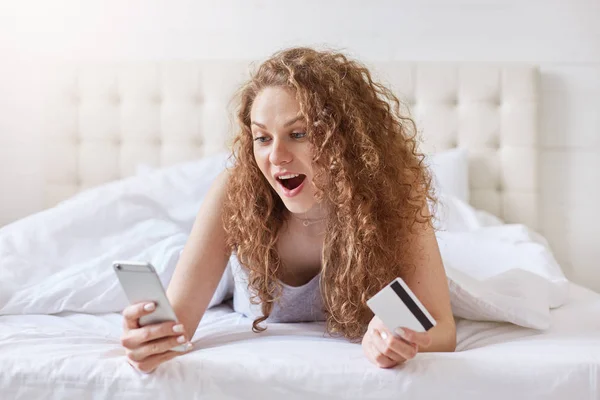 Shocked Relaxed Beautiful Woman Lies Bed Uses Modern Cell Phone — Stock Photo, Image