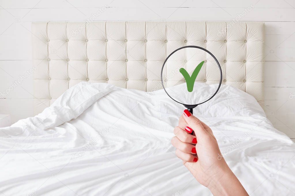 Everything in perfect and clean. Woman checks condition in hotel room, holds lens against white bed which demonstrates purity and tidiness. Whiteness concept