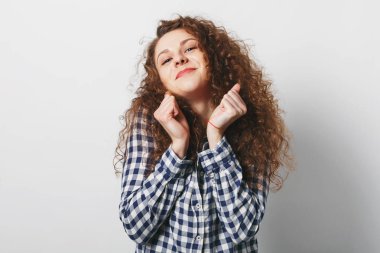 Memnun genç kadın model yumruklarını yükseltir ve sevinçle içine kamera, kayıtsızca, beyaz arka plan üzerinde izole giyinmiş görünüyor. Kıvırcık saçlı neşeli kadın ifade karşılamıştır. Olumlu duygular