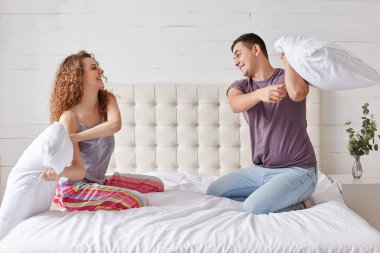 Genç aile çift uyku önce iyi eğlenceler, yatakta, aptal yastık ile birlikte mücadele. Güzel kız ve erkek arkadaşı yatak odasında oynamak, sevinçle gül. Zevk ve rahatlama kavramı