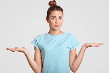 Tereddüt genç kadın uncertainy ile omuz silkiyor, karar veremiyorum, avuç içi tokalar, kamera, beyaz arka plan üzerinde izole mavi t gömlek giymiş clueless görünüyor. Peki, şimdi ne yapacağız?