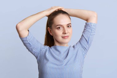 Hoş görünümlü genç kadın modeli at kuyruğu yapar, çizgili şık bluz giyer, Studio mavi arka plan teşkil etmektedir, kendinden emin bir ifadeyle kameraya benziyor. İnsanlar ve güzellik kavramı