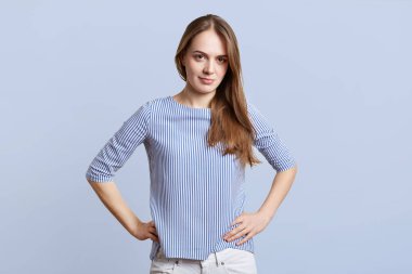 Oldukça şık giyim kadın yatay atış eller bel üzerinde tutar, kendinden emin ve kararlı expressionn ile kamera görünüyor, mavi arka planı teşkil etmektedir. Kadın kendini emin olmak